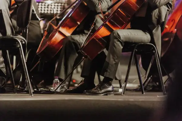 Orkiestra grająca muzykę filmową. Widoczne fragmenty instrumentów i eleganckie buty muzyków.
