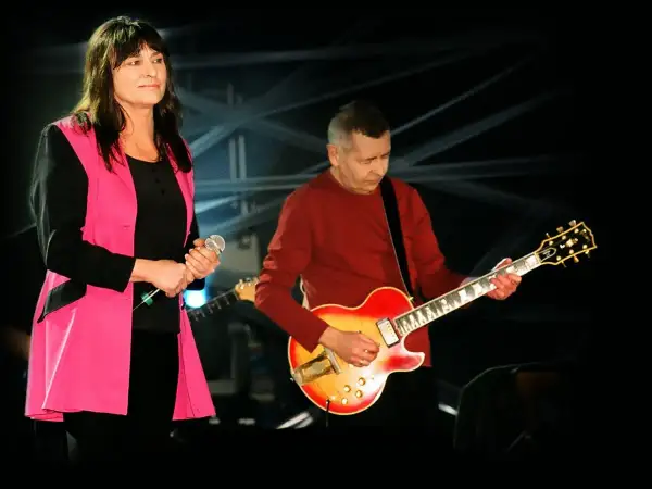 Kobieta z mikrofonem i mężczyzna grający na gitarze, członkowie zespołu Breakout, na scenie.