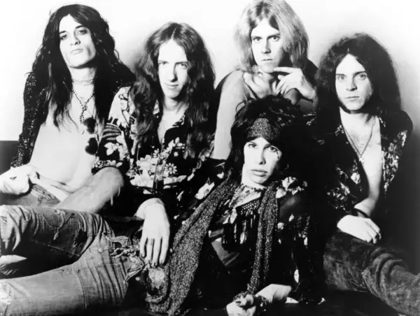 Aerosmith członkowie w rockowym stylu, z długimi włosami i charakterystycznymi strojami.