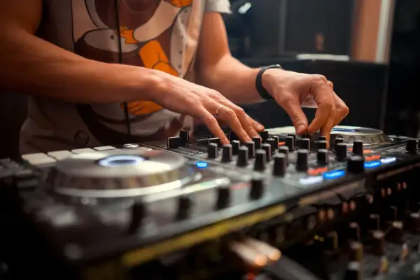 Dłonie DJ-a miksujące muzykę na sprzęcie. Widać pierścionek na palcu i zegarek. To polscy DJ-e tworzą rytm.