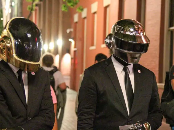 Daft Punk członkowie w złotych i srebrnych hełmach, ubrani w garnitury, idą ulicą.