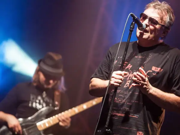 Wokalista Budki Suflera śpiewa na koncercie. W tle basista gra na gitarze. Piosenki Budki Suflera alfabetycznie to ich bogaty repertuar.