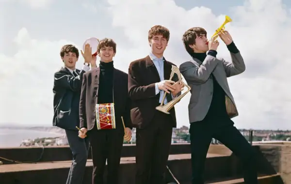 The Beatles w swoich eleganckich garniturach, grając na instrumentach, tworzą radosną atmosferę, jakby zapowiadali nowe utwory.